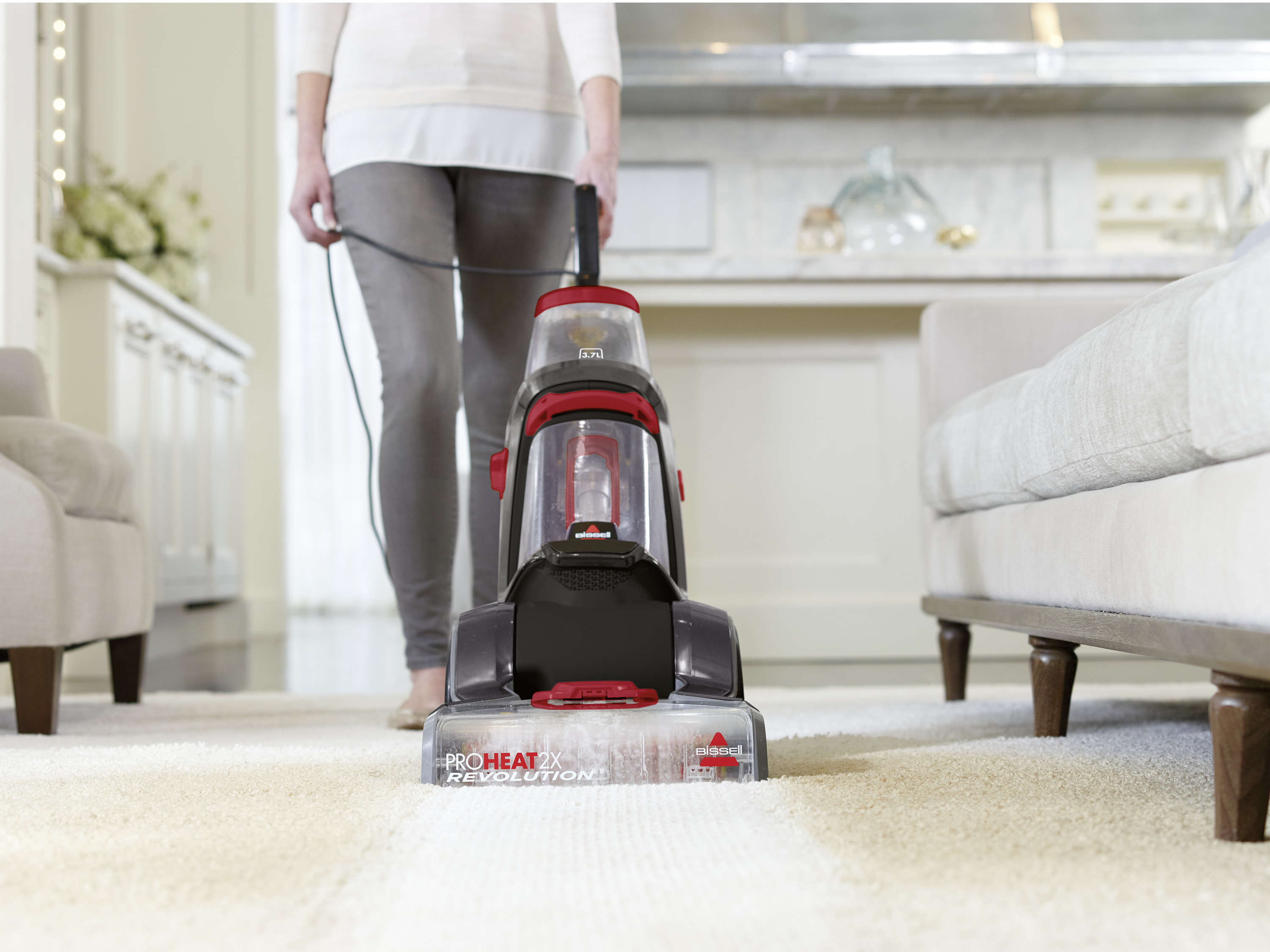 Eine Frau, die einen Teppich mit einem Bissell ProHeat 2X Revolution Staubsauger saugt. Der Teppich ist beige.