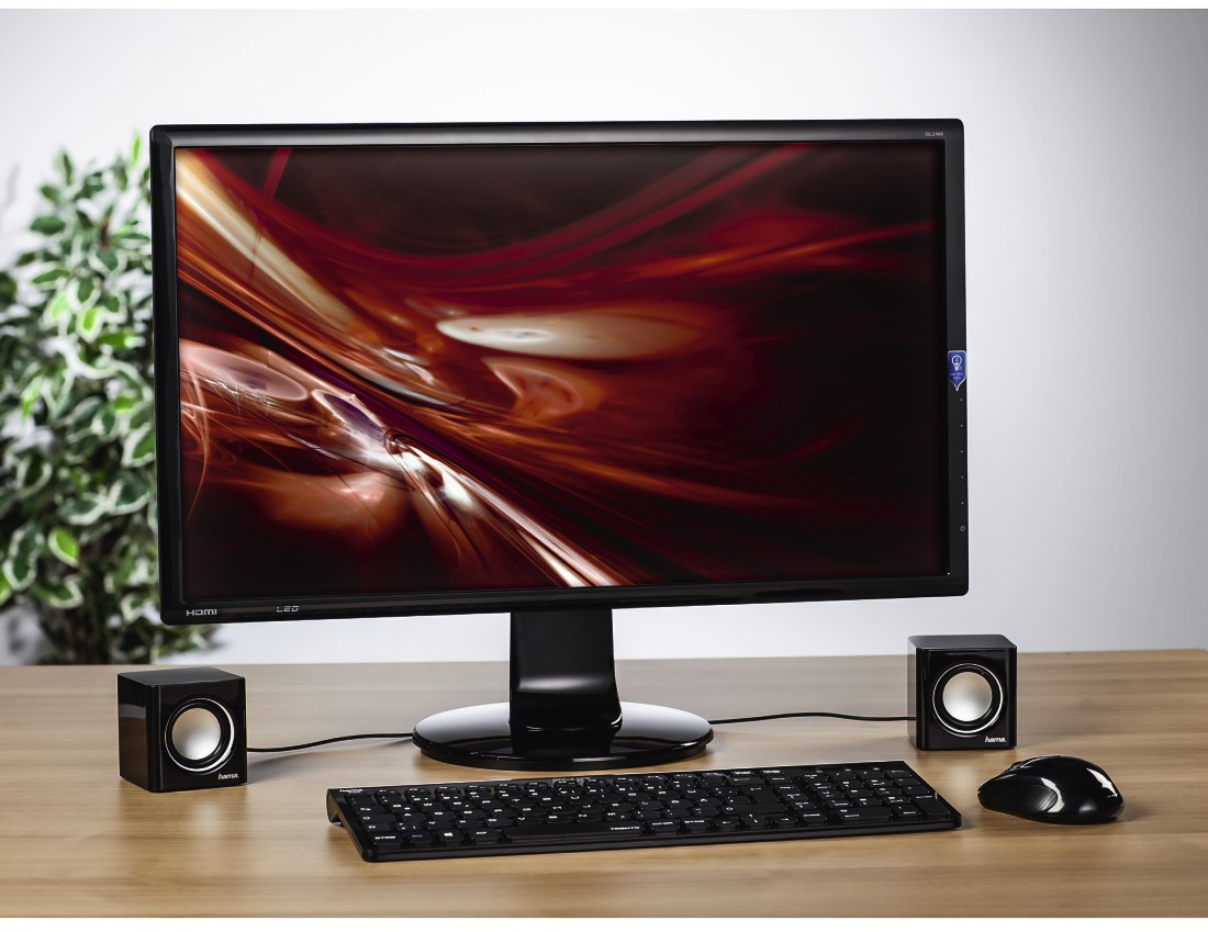 Computeropstelling met monitor, luidsprekers, toetsenbord en muis op een houten bureau.