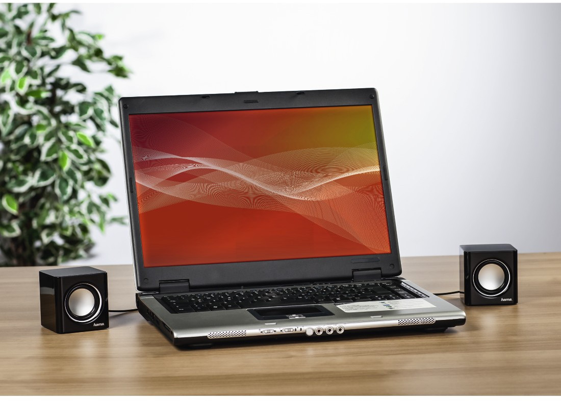 Laptop met luidsprekers op een houten tafel, met een rood en geel scherm.