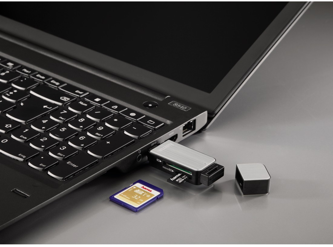 Ordinateur portable avec une carte SD et un lecteur de carte USB insérés, avec un autre lecteur à proximité.