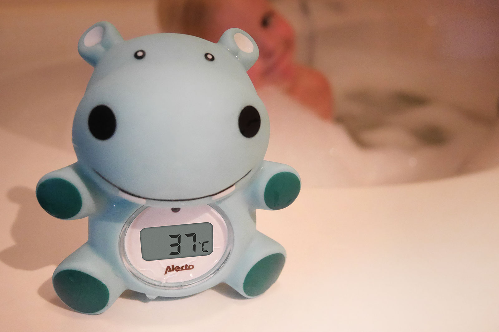 Blue hippo bath thermometer displaying 37°C, with a person in the background.