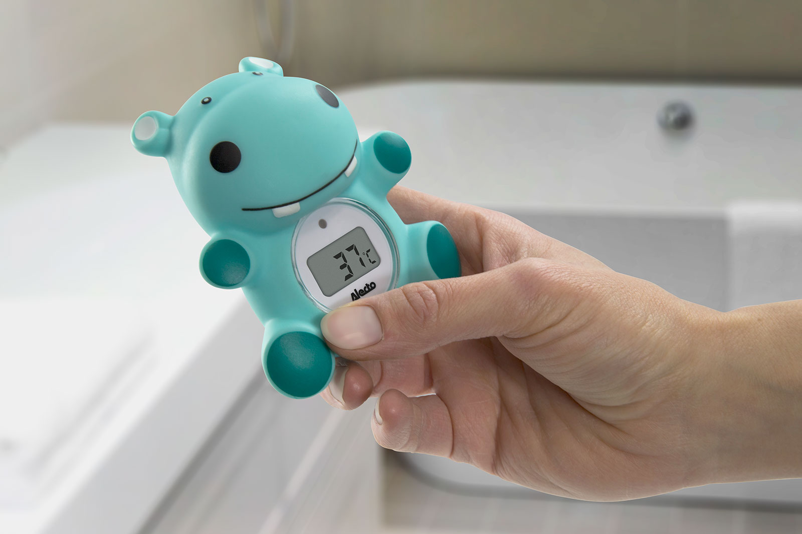 Hand holding a teal hippo-shaped bath thermometer, displaying 37°C.