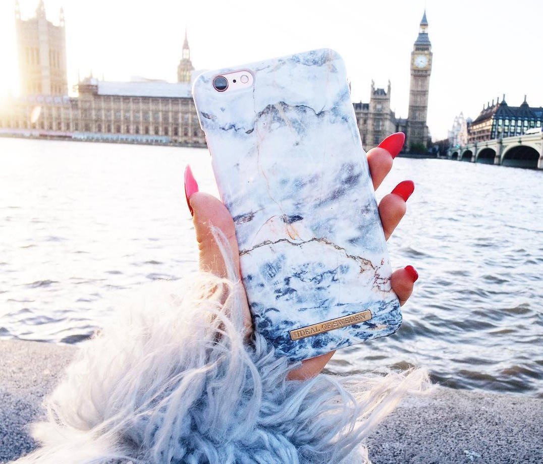 Hand hält Marmor-Handyhülle mit roten Nägeln, Big Ben im Hintergrund, Fluss und Himmel.