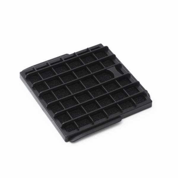 A black rectangular filter with a grid pattern and a porous interior rests on a white background. The filter is slightly angled.