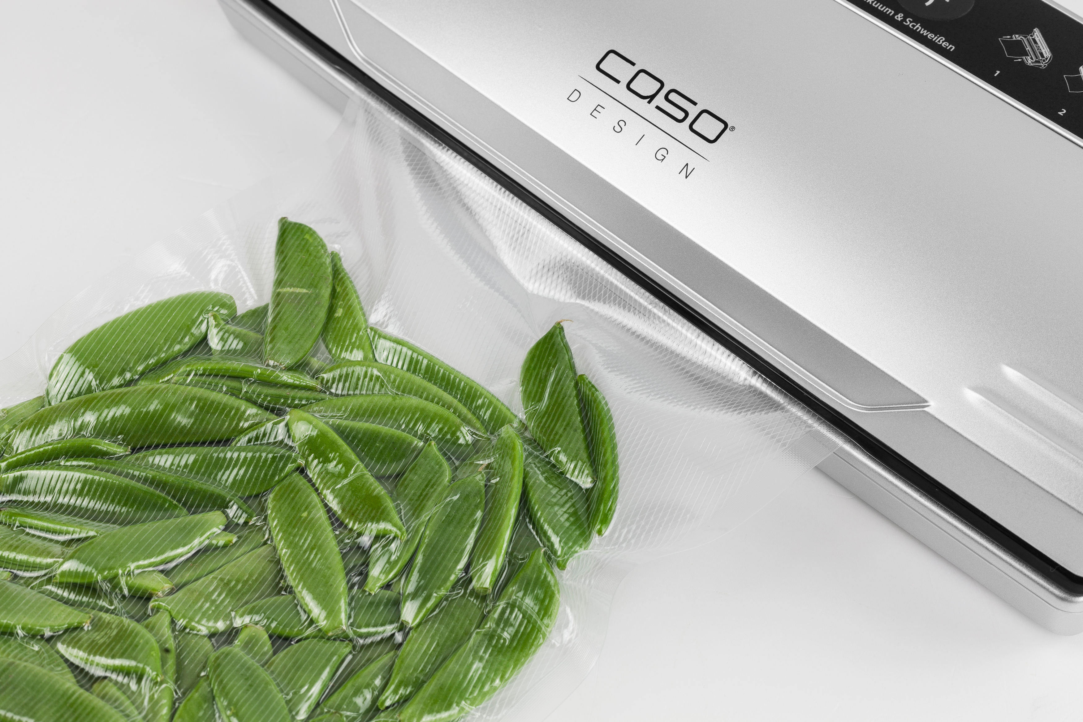 Vakuumiergerät mit Beutel mit grünen Zuckerschoten, auf weißer Oberfläche versiegelt.