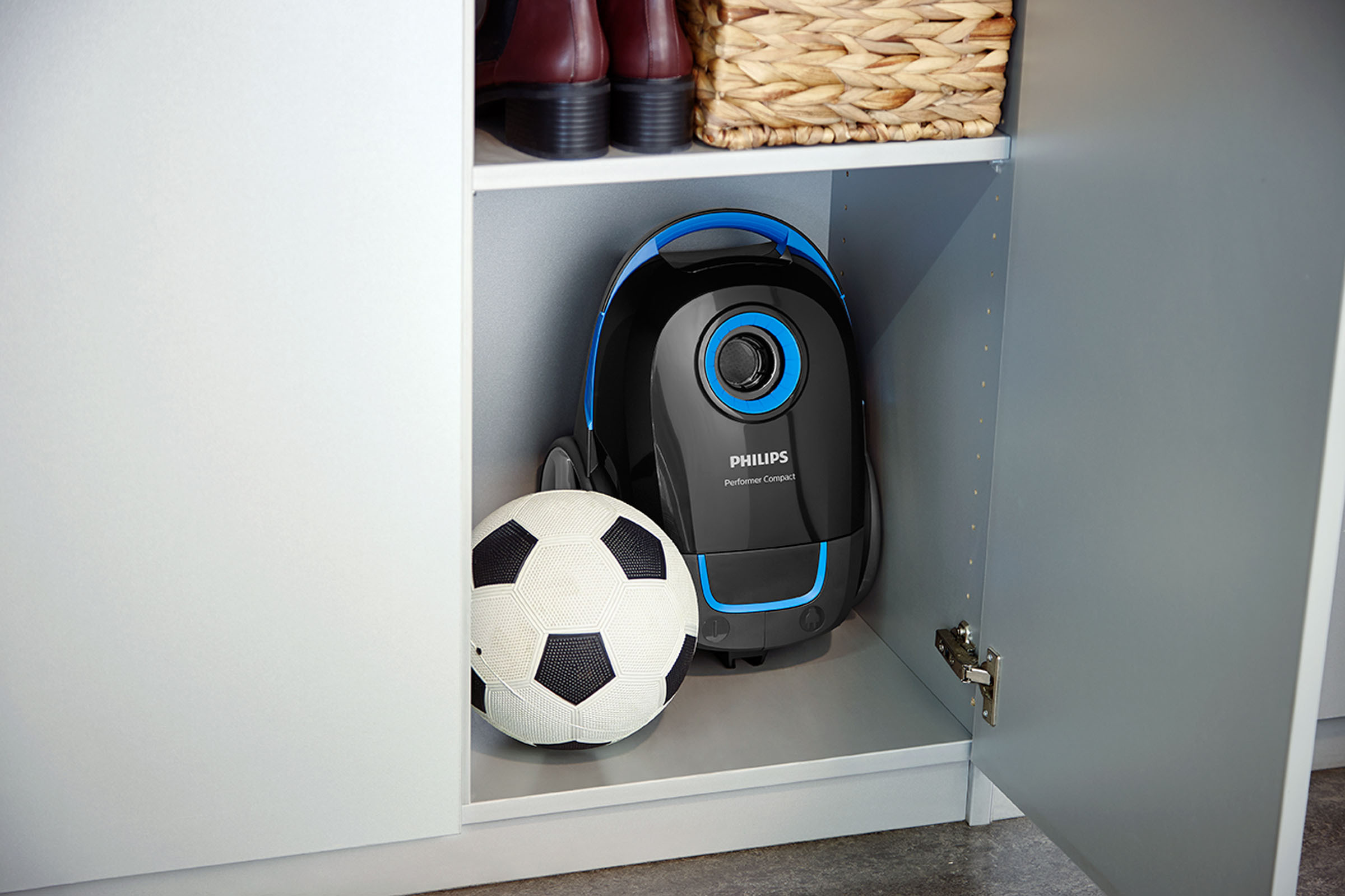 Ein schwarzer und blauer Staubsauger, ein Fußball und Stiefel befinden sich in einem Schrank.