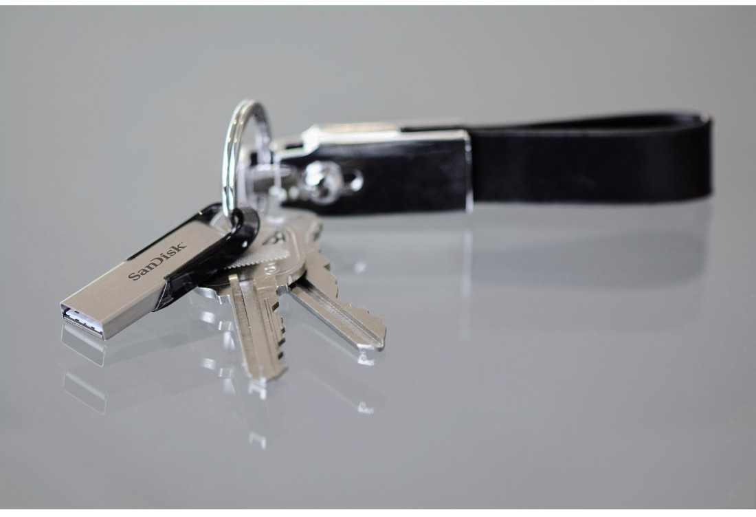 Clés et une clé USB argentée attachées à un porte-clés en cuir noir, posées sur une surface grise.