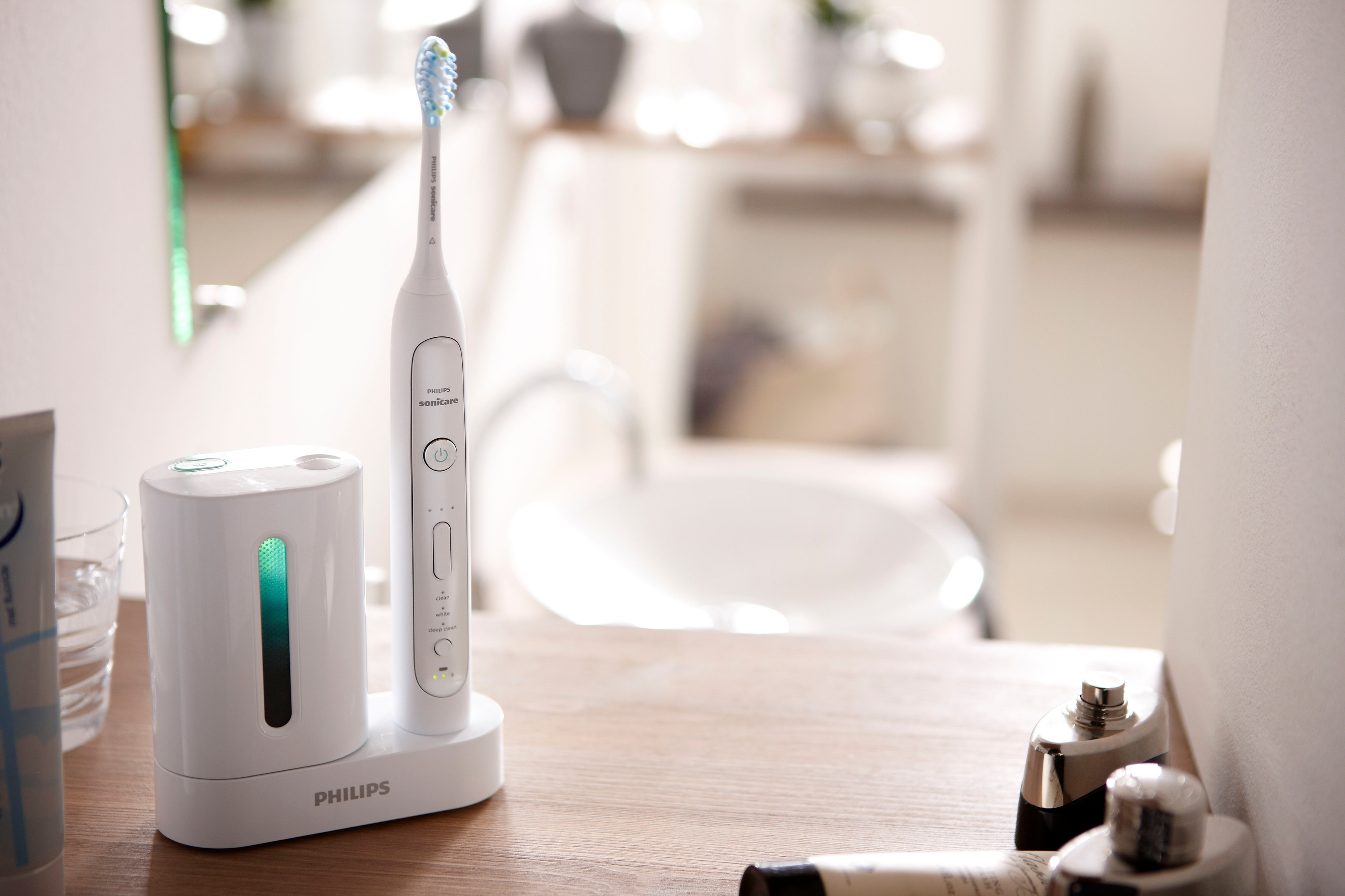 Weiße Philips Sonicare Zahnbürste und Ladestation auf Holzoberfläche mit Badezimmerartikeln.