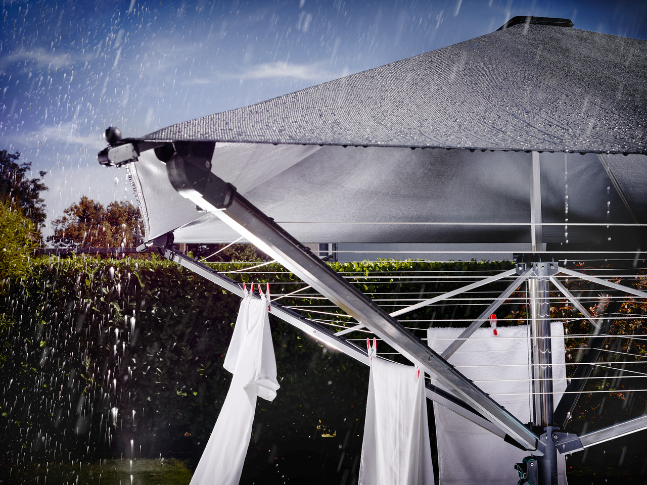Wäsche trocknet im Regen auf einer Wäschespinne. Dunkler Himmel.