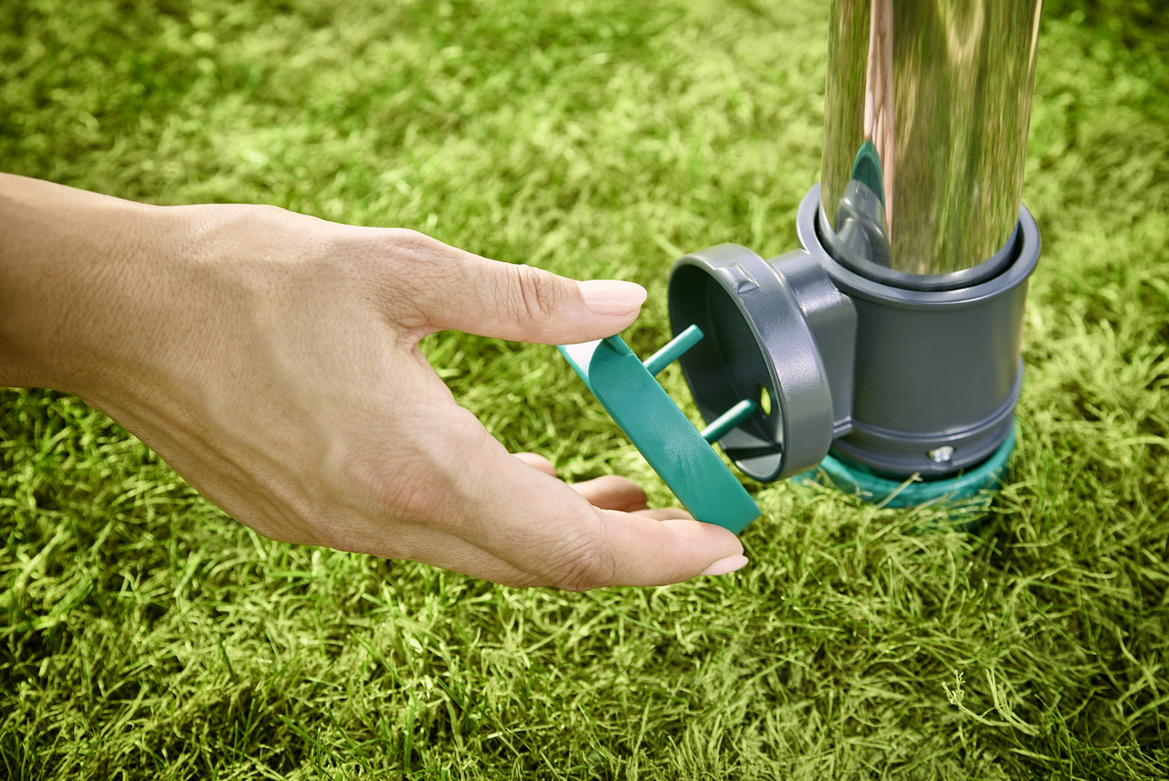 Eine Hand platziert ein grünes Teil in ein Sprinklersystem. Das System befindet sich in grünem Gras.