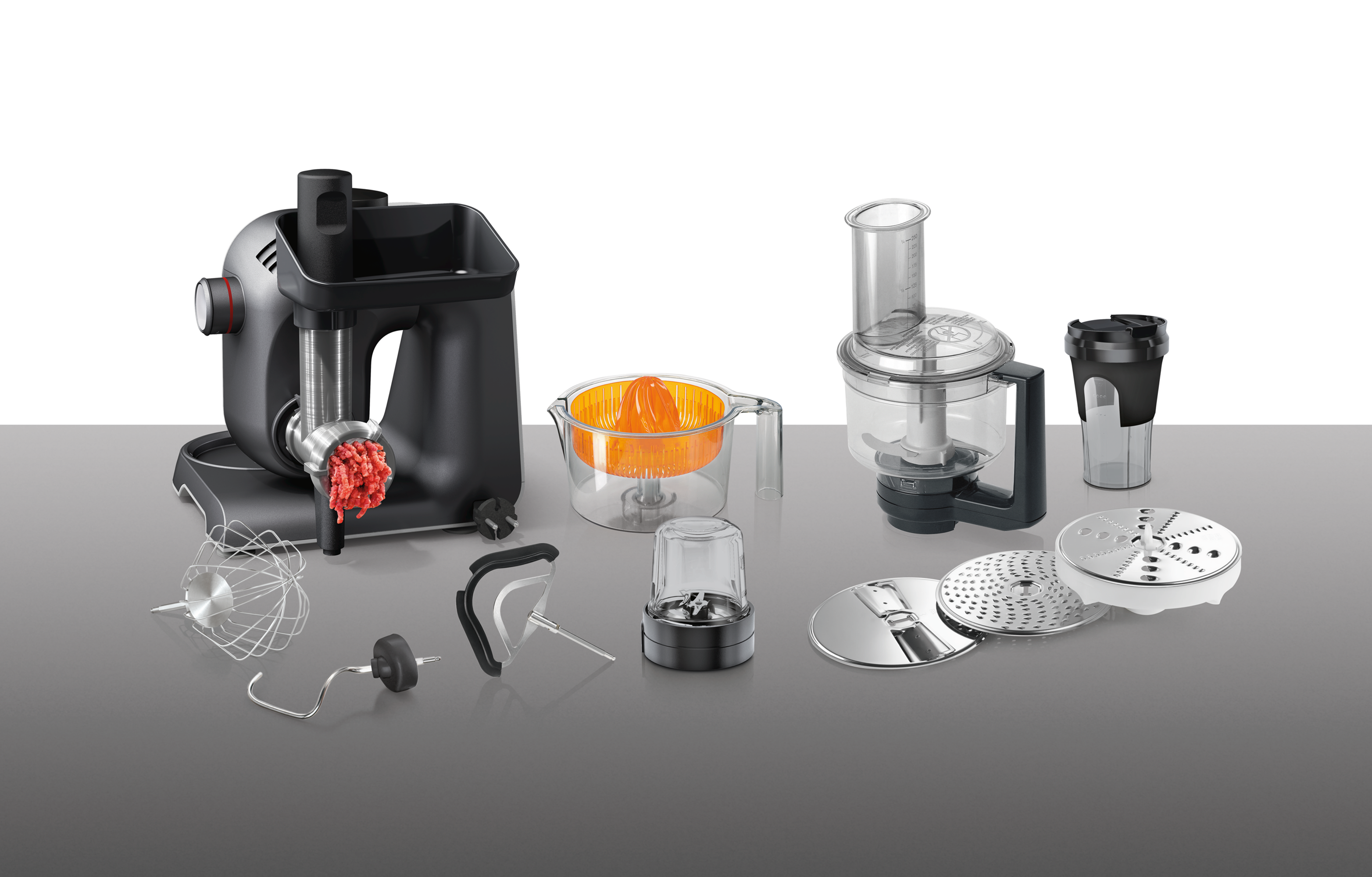 Variety of kitchen appliance attachments on a white surface.  Meat grinder, juicer, food processor.