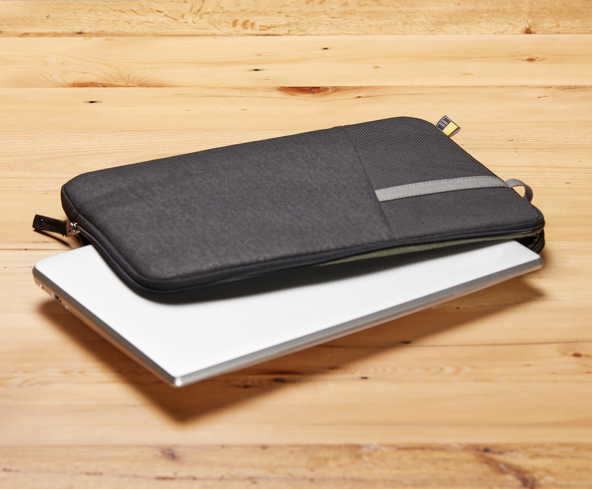 A laptop sits inside a black laptop sleeve lying on a wood surface.