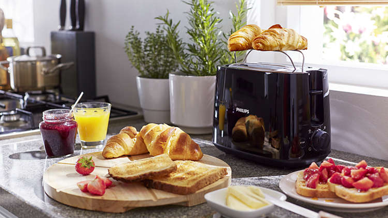Egy reggeli jelenet kenyérpirítóval, croissant-okkal, pirítóssal, lével, lekvárral és eperrel.