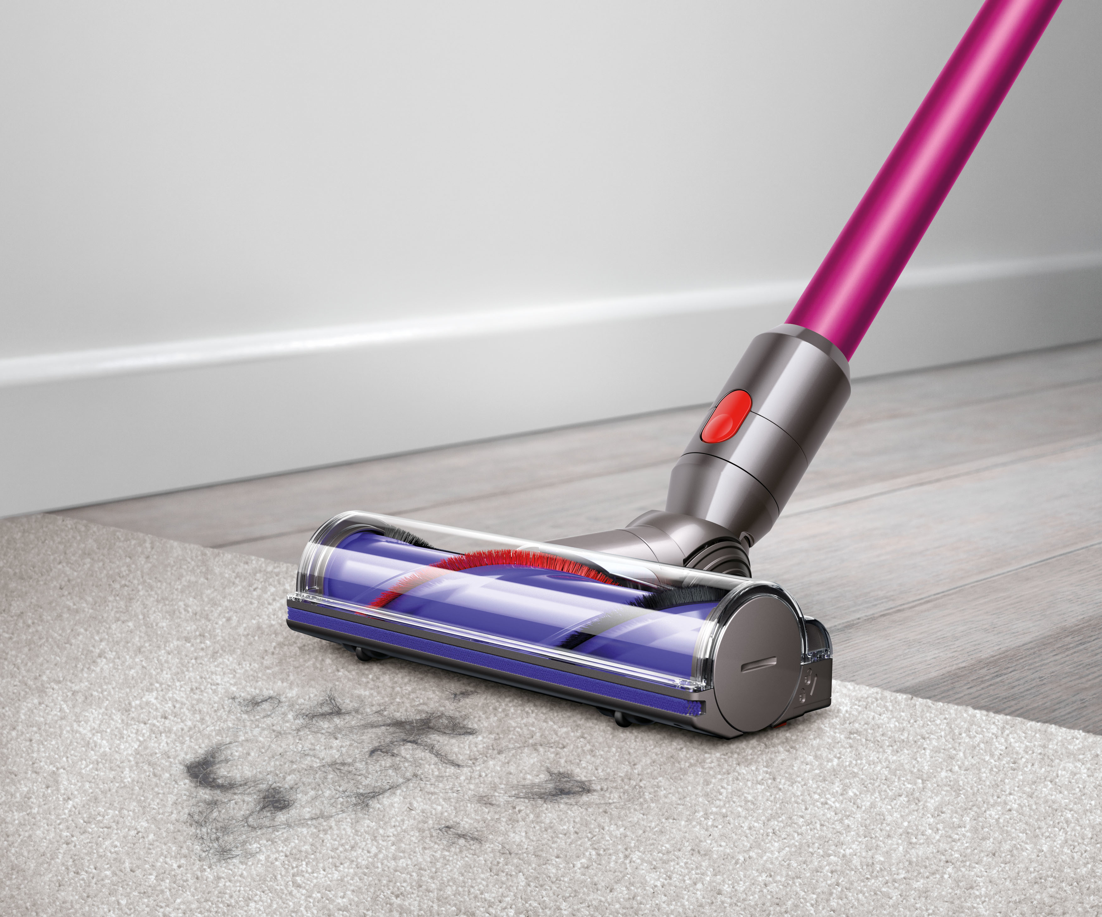 Ein rosa Staubsauger reinigt einen Teppich mit Schmutz. Im Hintergrund sind eine weiße Wand und ein Holzboden.
