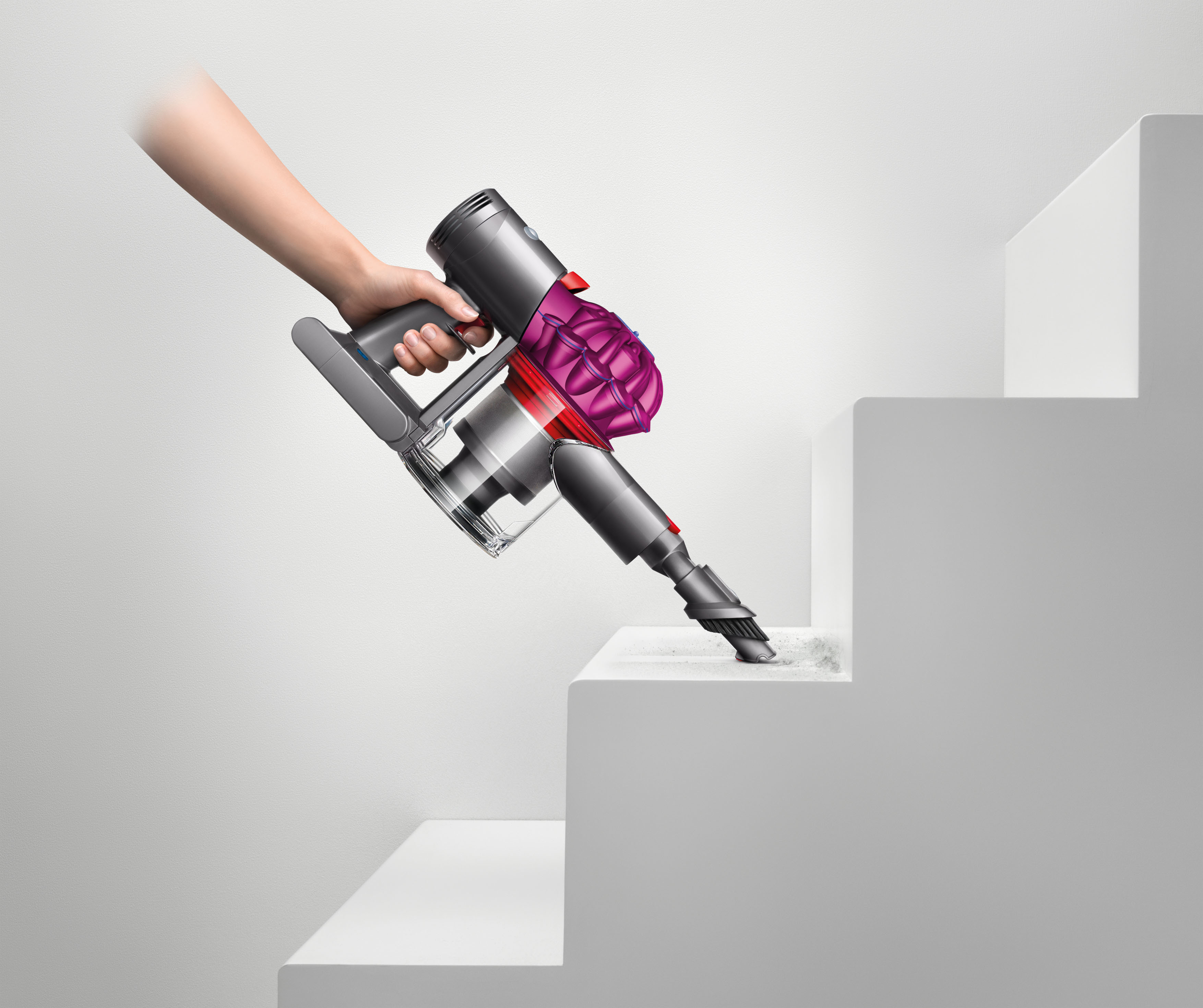 Eine Hand hält einen Dyson-Staubsauger und reinigt eine weiße Treppe. Der Staubsauger ist grau und magenta.