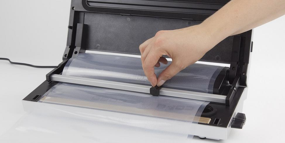Eine Hand bedient ein Vakuumiergerät für Lebensmittel, indem sie einen Beutel in die Maschine legt.