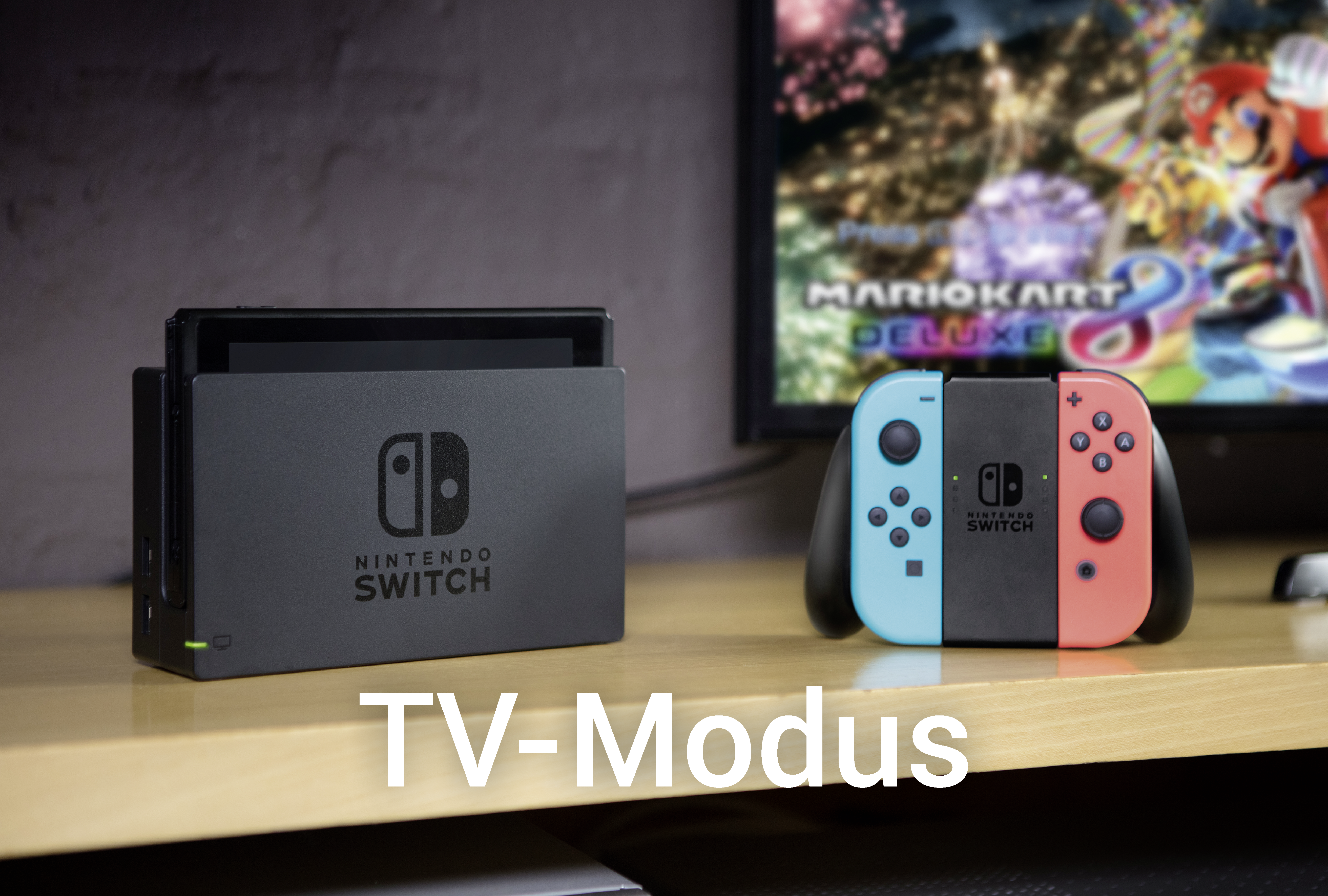 Nintendo Switch Konsole und Controller auf einem Holztisch, mit Fernseher im Hintergrund. Text 'TV-Modus'.