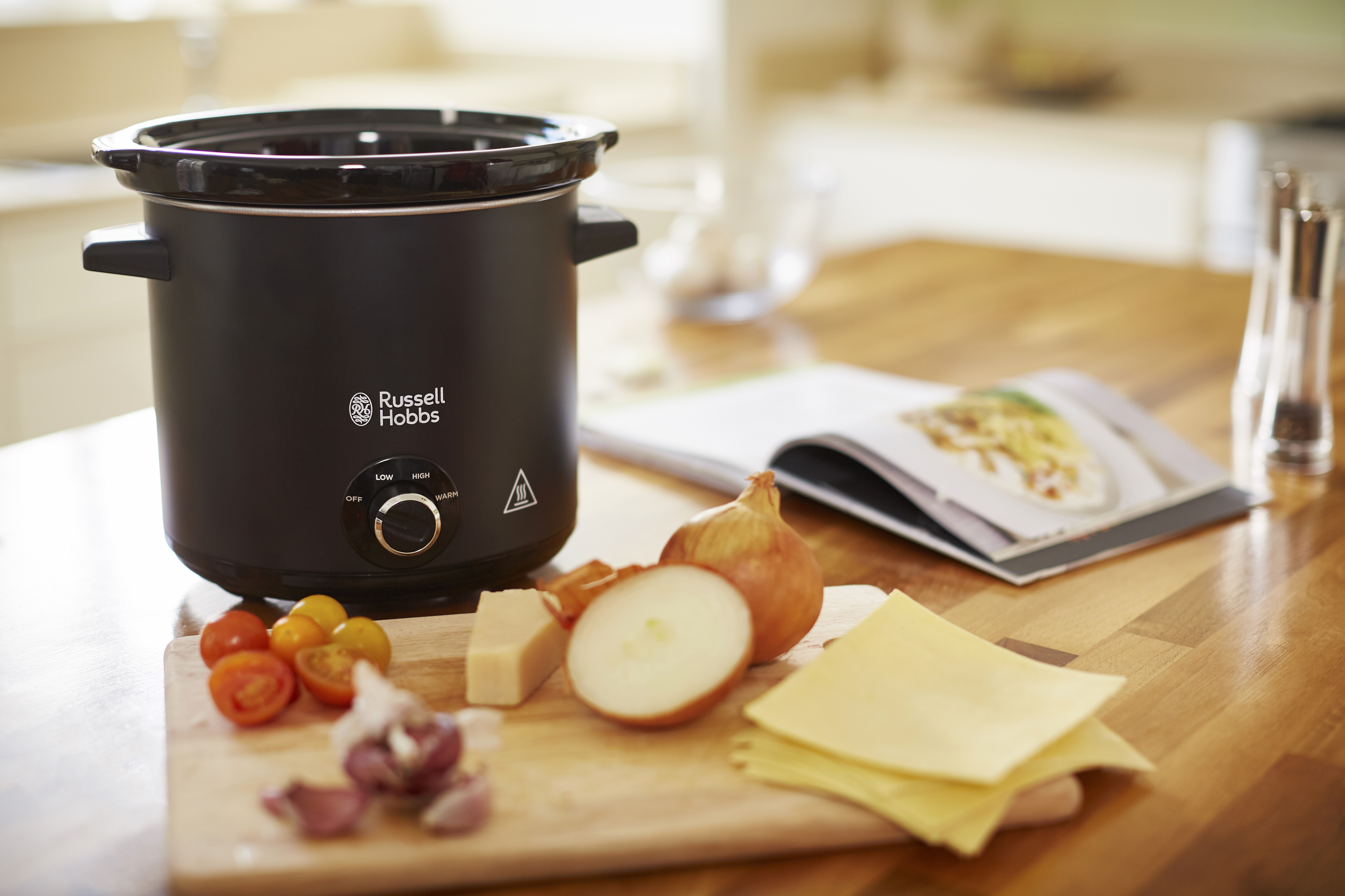 Een zwarte Russell Hobbs slowcooker met ingrediënten op een houten snijplank.