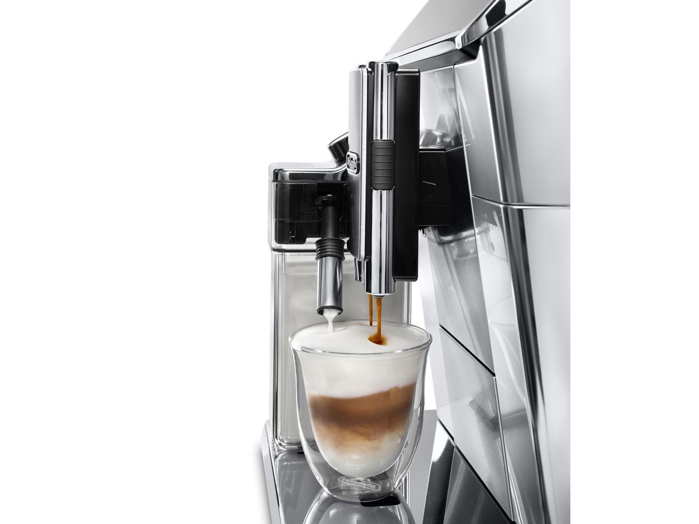A coffee machine dispensing coffee and milk into a glass. The glass has layers of coffee, milk, and foam. Machine is silver.