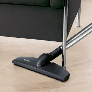 A black vacuum head under a chair, on light wood floor.