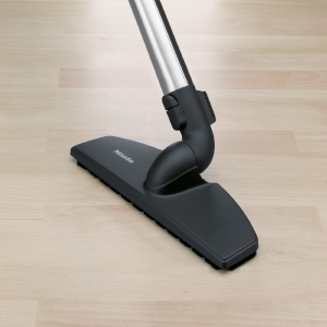 Vacuum cleaner head on wooden floor. Black brush, metallic tube.