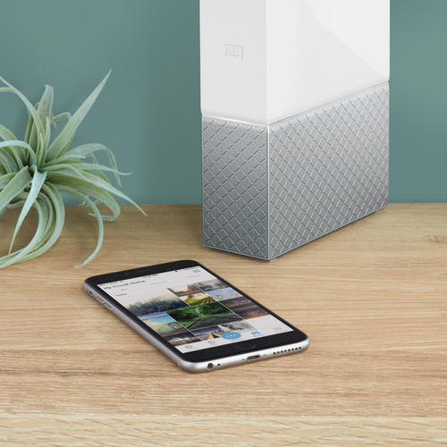 A smartphone displaying a photo gallery rests on a wooden surface, near a white data storage device.