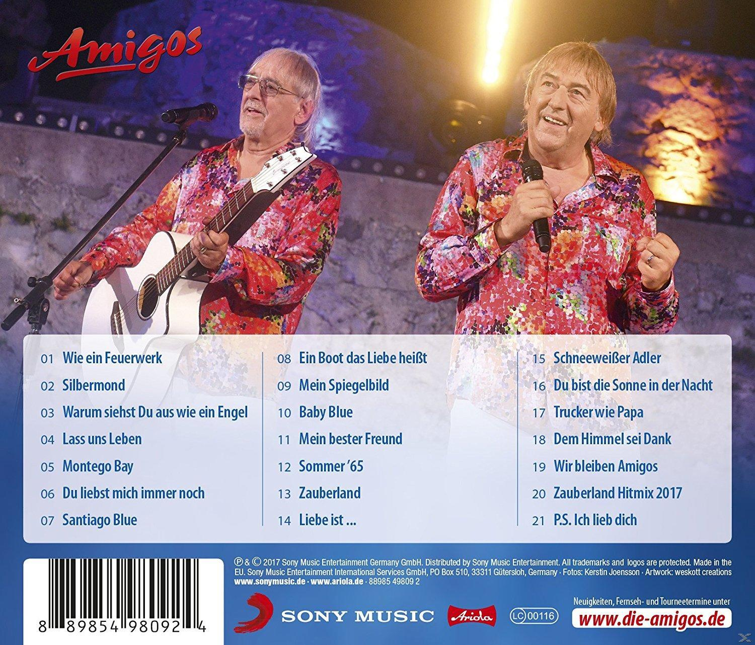 Twee mannen op het podium met microfoons en een gitaar. Ze dragen kleurrijke shirts. De achtergrond toont een podium.