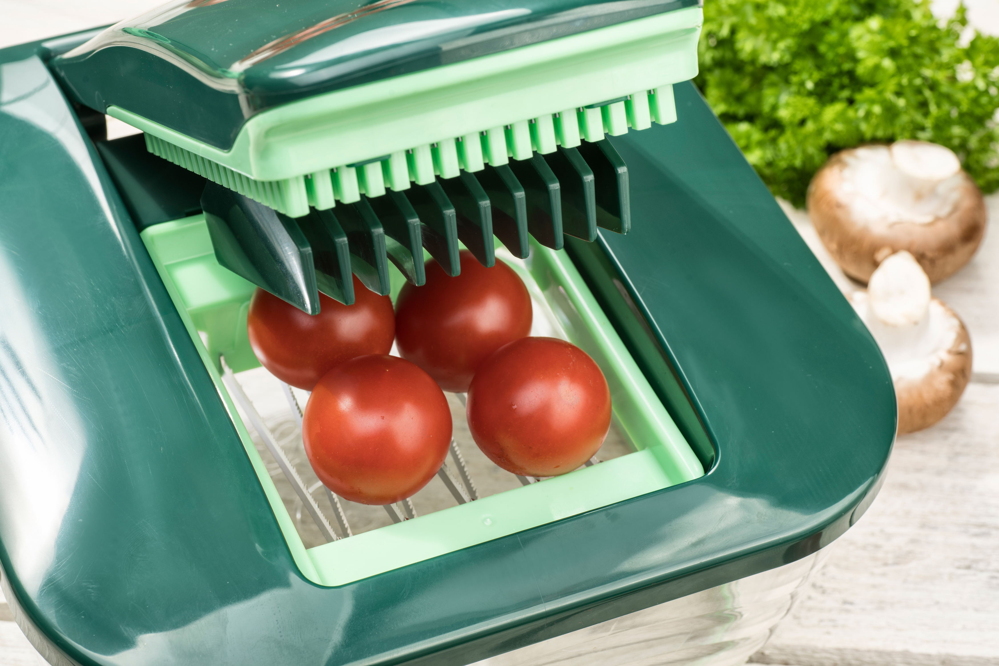 Grüner Gemüseschneider mit Tomaten. Pilze und Petersilie im Hintergrund.