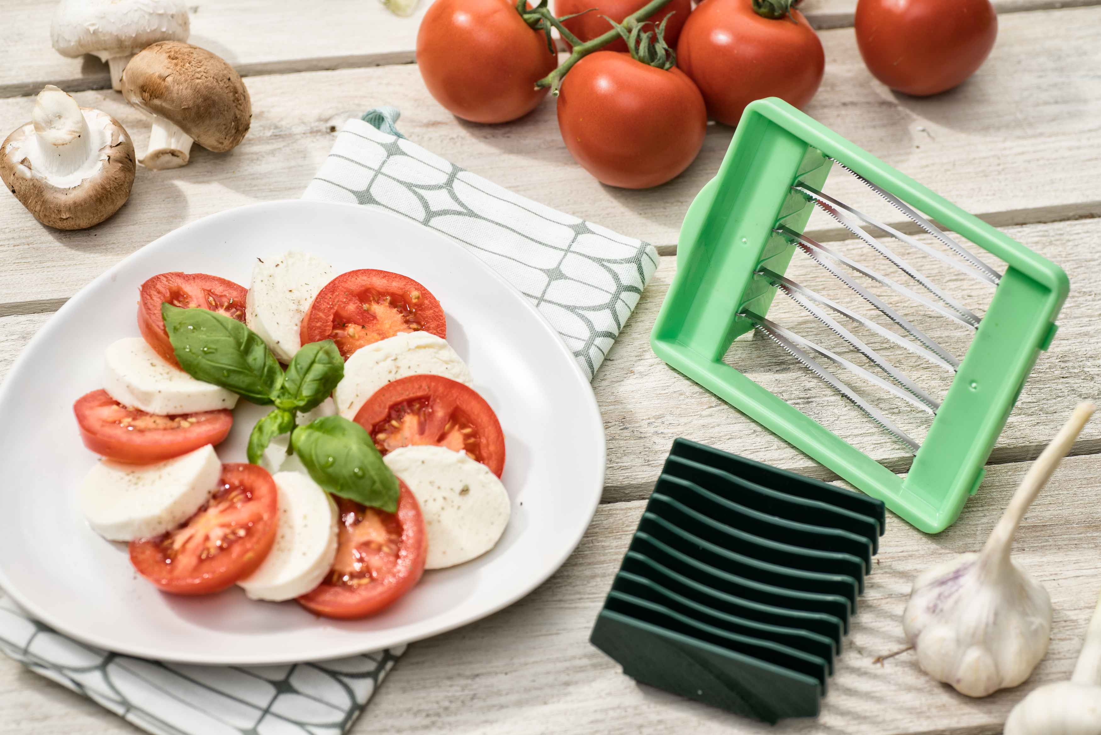 Teller mit Tomaten und Mozzarella mit Basilikum, neben Gemüse und Schneider.