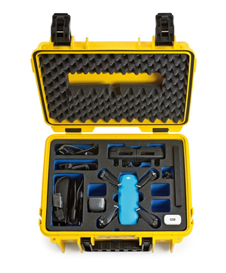 Open gele koffer met blauwe drone en accessoires. Schuimrubber beschermt de drone. Zwarte sluitingen zekeren de koffer.