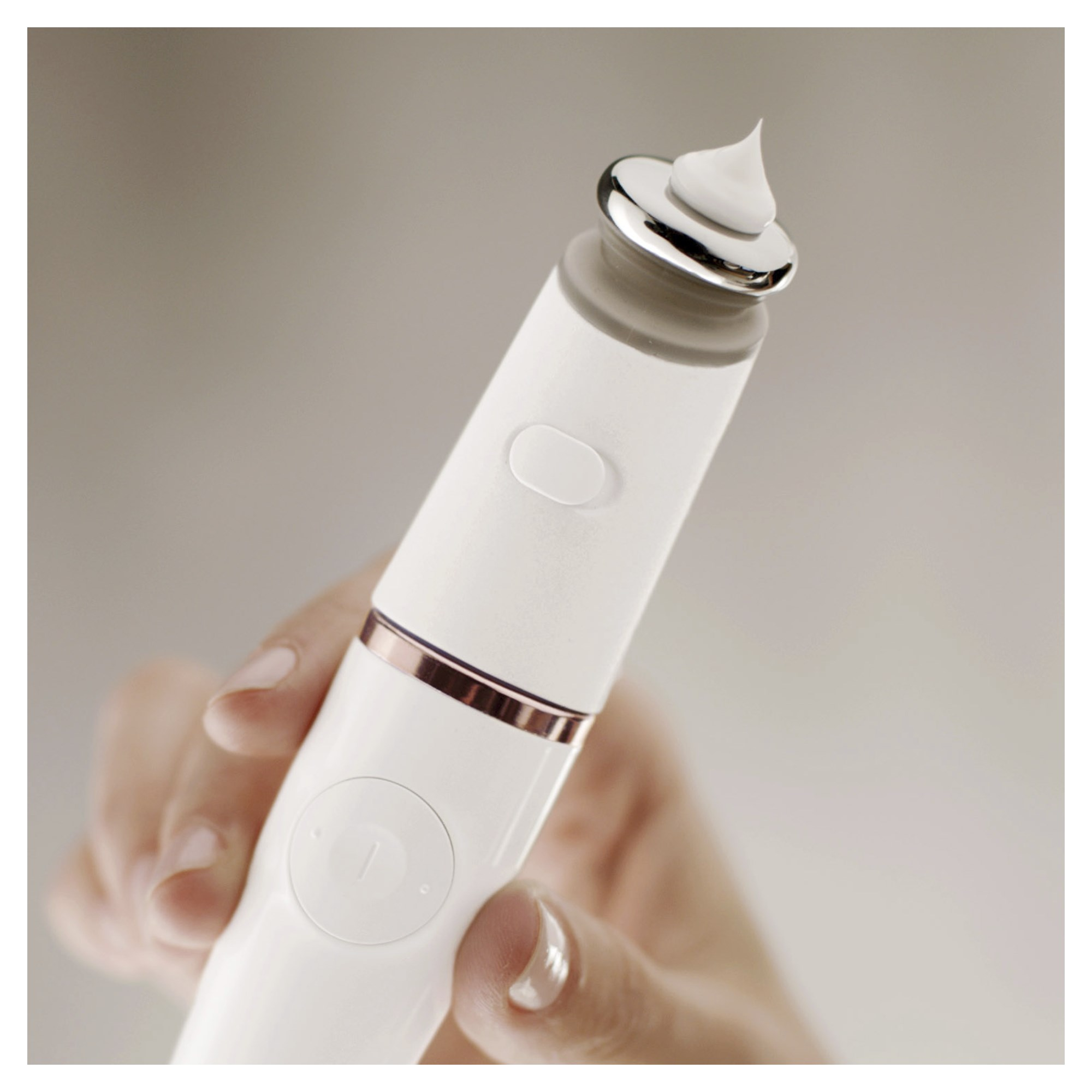 Un appareil de beauté blanc tenu par une main. Il y a une petite quantité de crème sur la pointe.