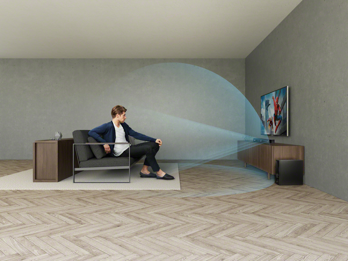 Mann sitzt und schaut fern. Der Fernseher zeigt eine Spider-Man-Szene. Soundsystem darunter.