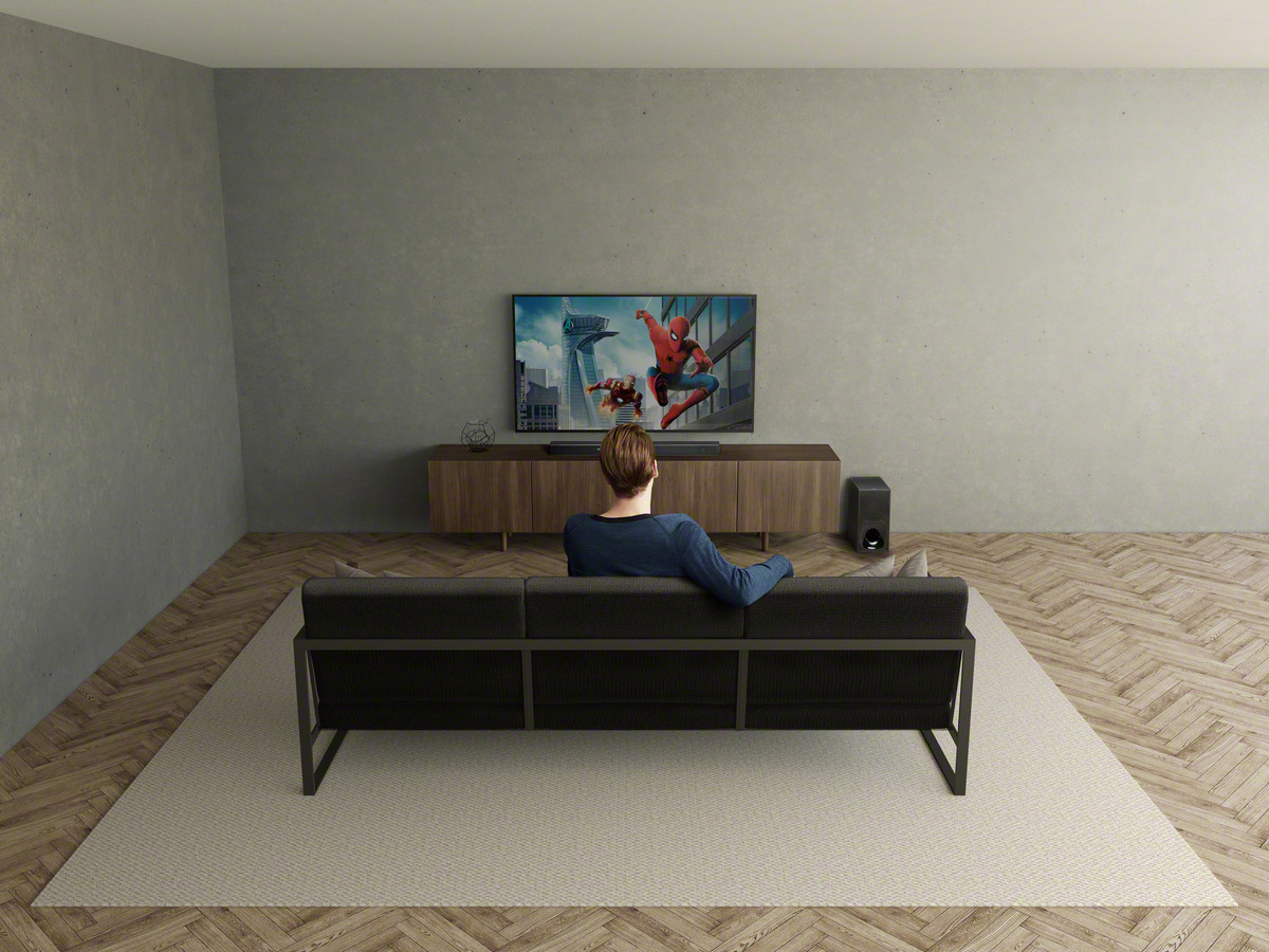 Mann sitzt auf Couch und schaut TV. TV zeigt Spider-Man. Neutralfarbiger Raum.