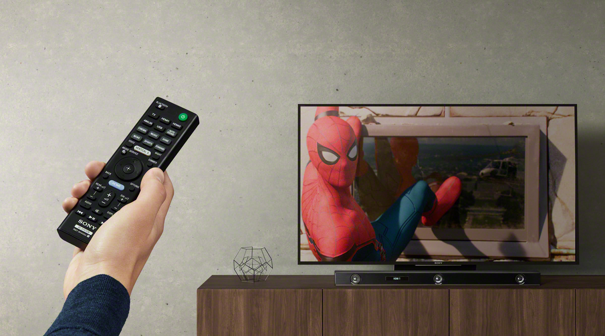 Eine Hand mit Fernbedienung steuert einen Fernseher mit Spiderman.