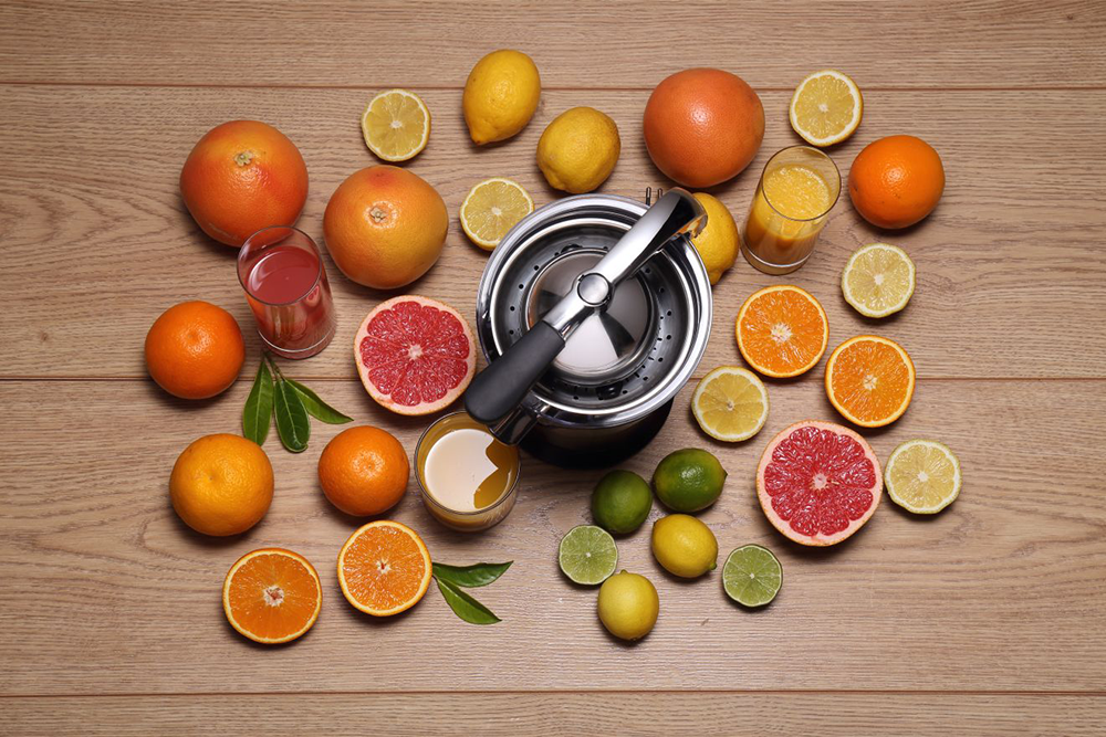 Egy asztal citrusfélékkel, gyümölcslé-poharakkal és egy gyümölcsfacsaróval. A gyümölcsök narancs, citrom és grapefruit.
