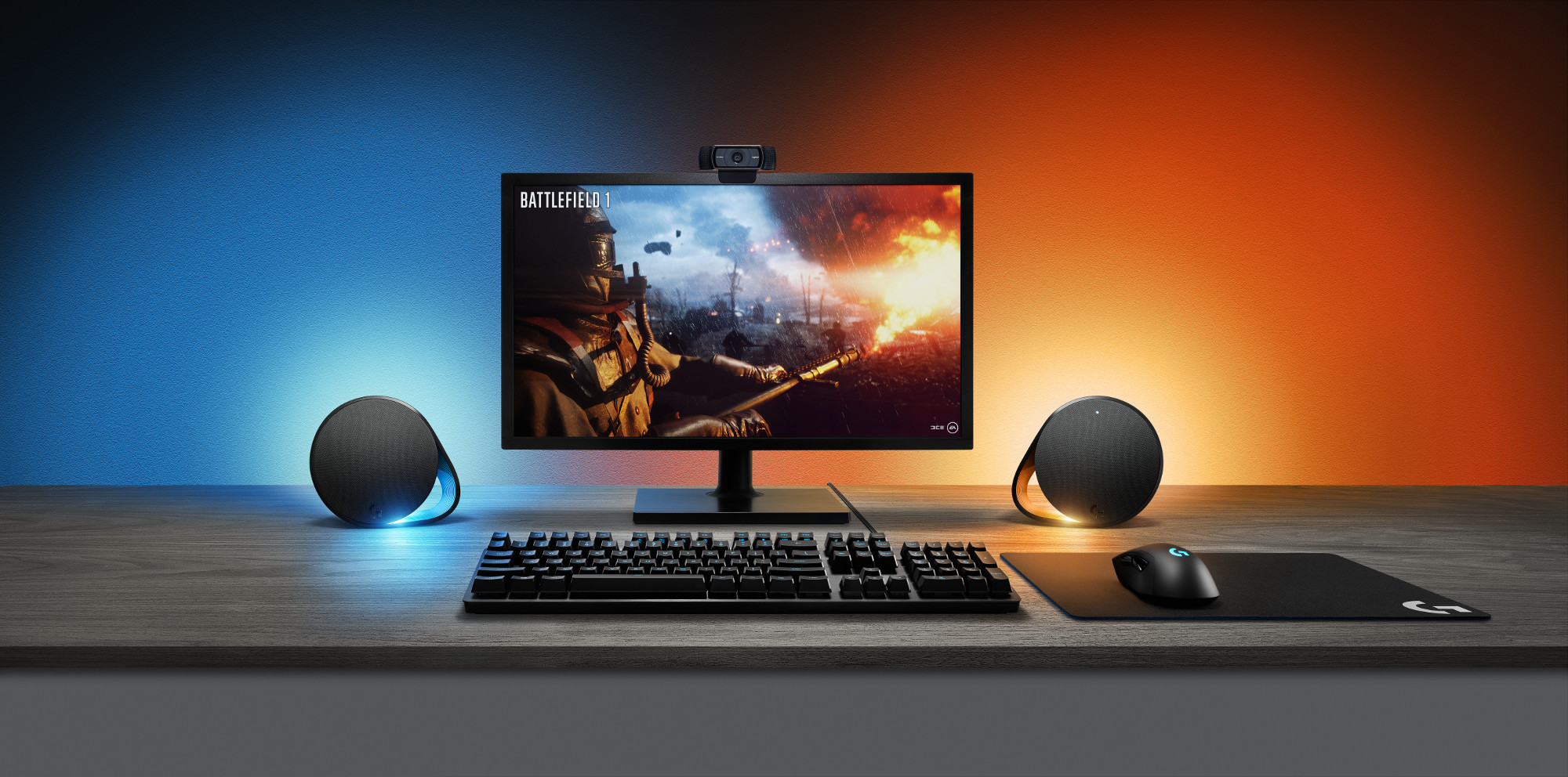 Gaming-opstelling met een monitor, toetsenbord, muis en luidsprekers in een blauw en oranje verlichte kamer.