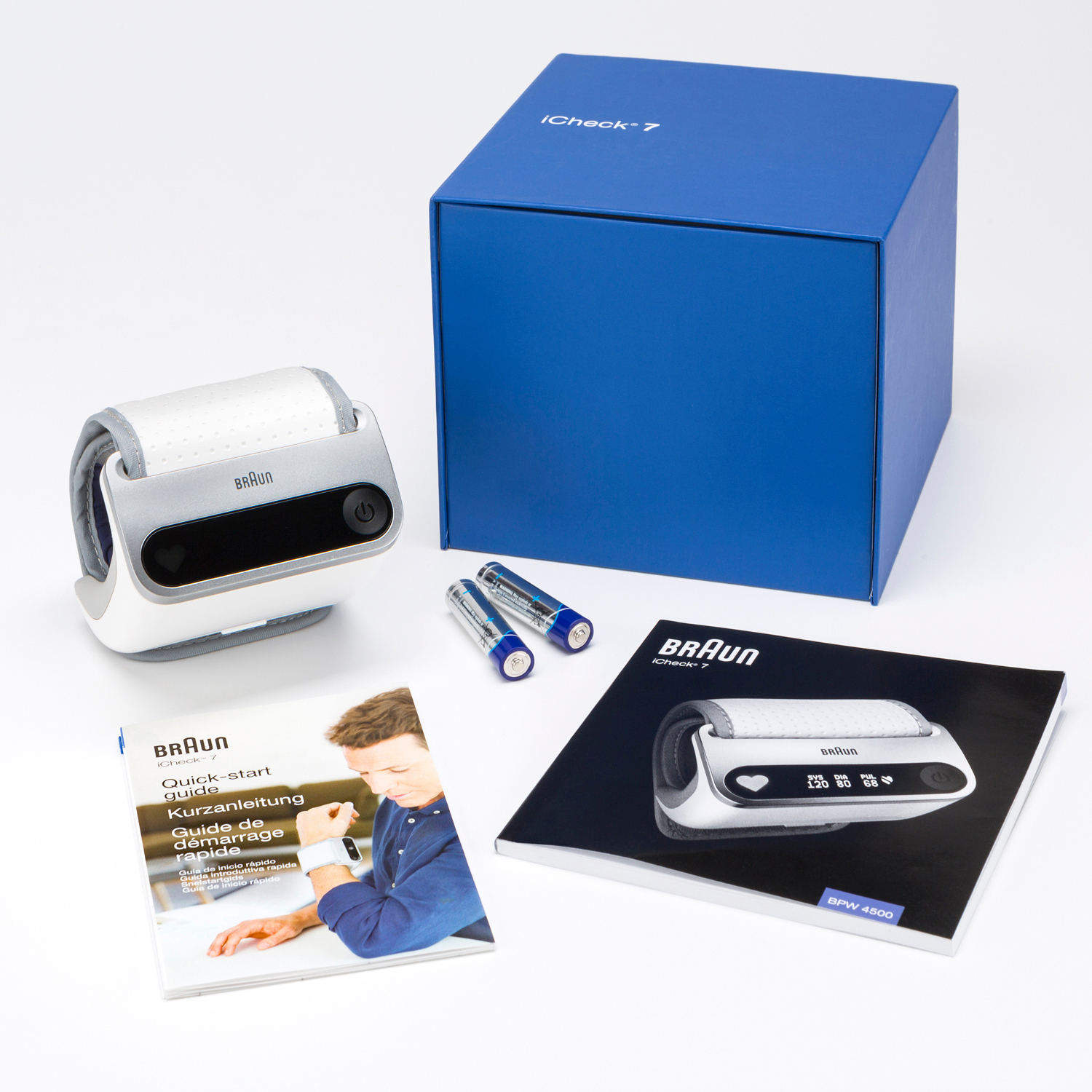 Kit de tensiomètre avec moniteur, boîte, piles et manuels sur une surface blanche.