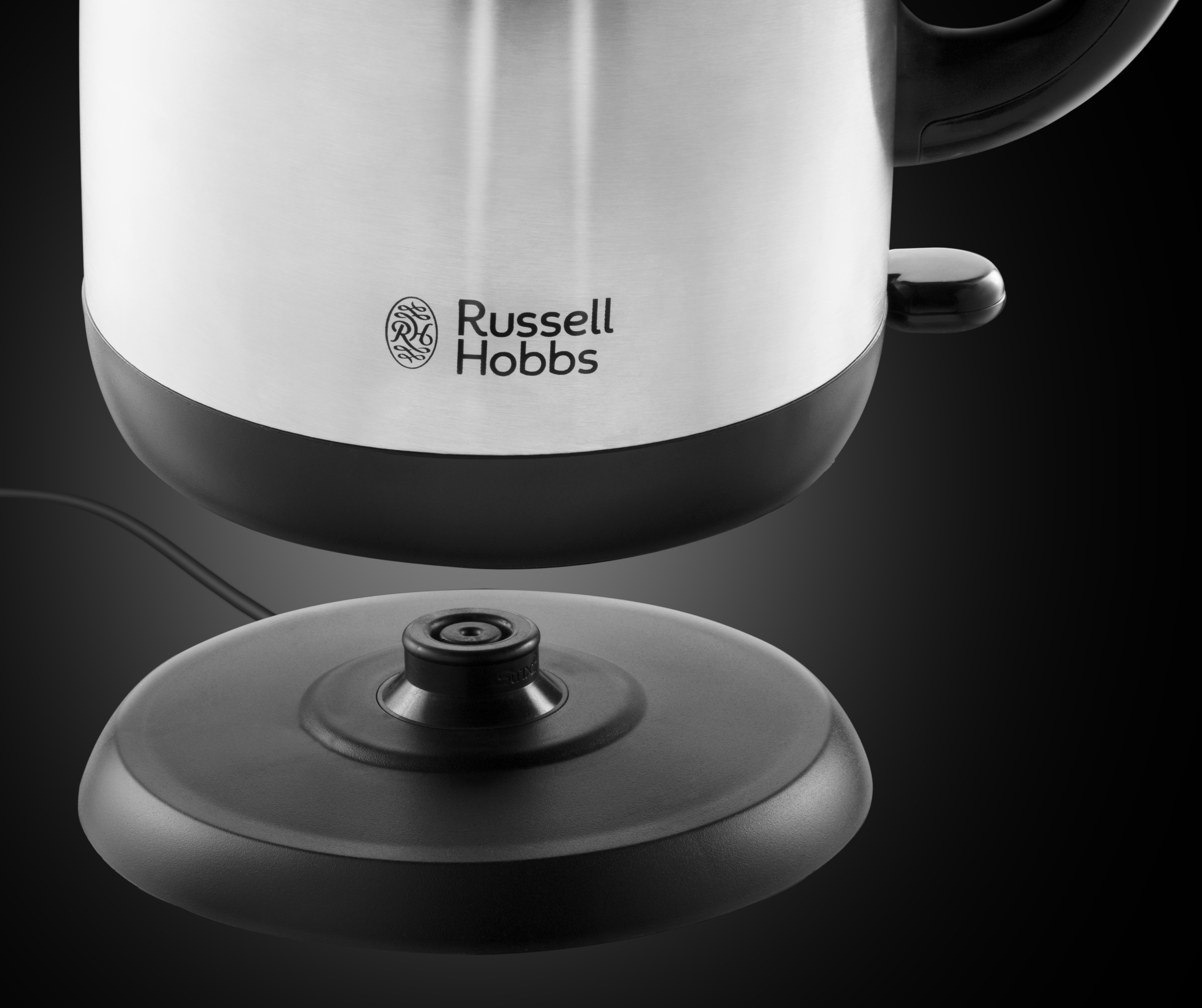 Egy rozsdamentes acél és fekete Russell Hobbs vízforraló fekete talpon, a logó látható.