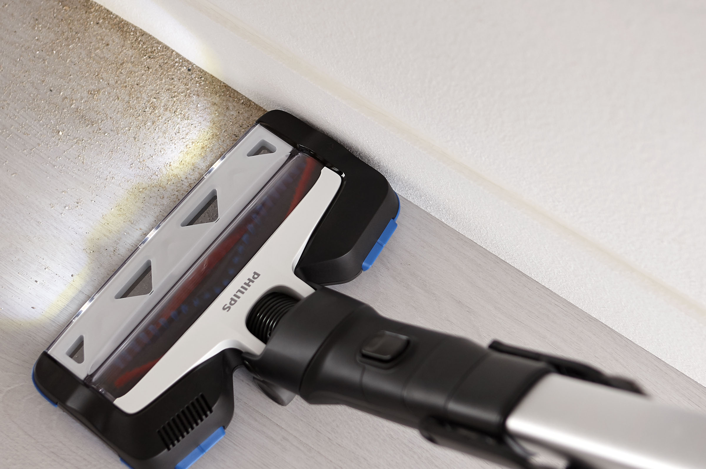 Ein Philips-Staubsaugerkopf reinigt einen staubigen Boden. Der Hintergrund zeigt eine weiße Wand.
