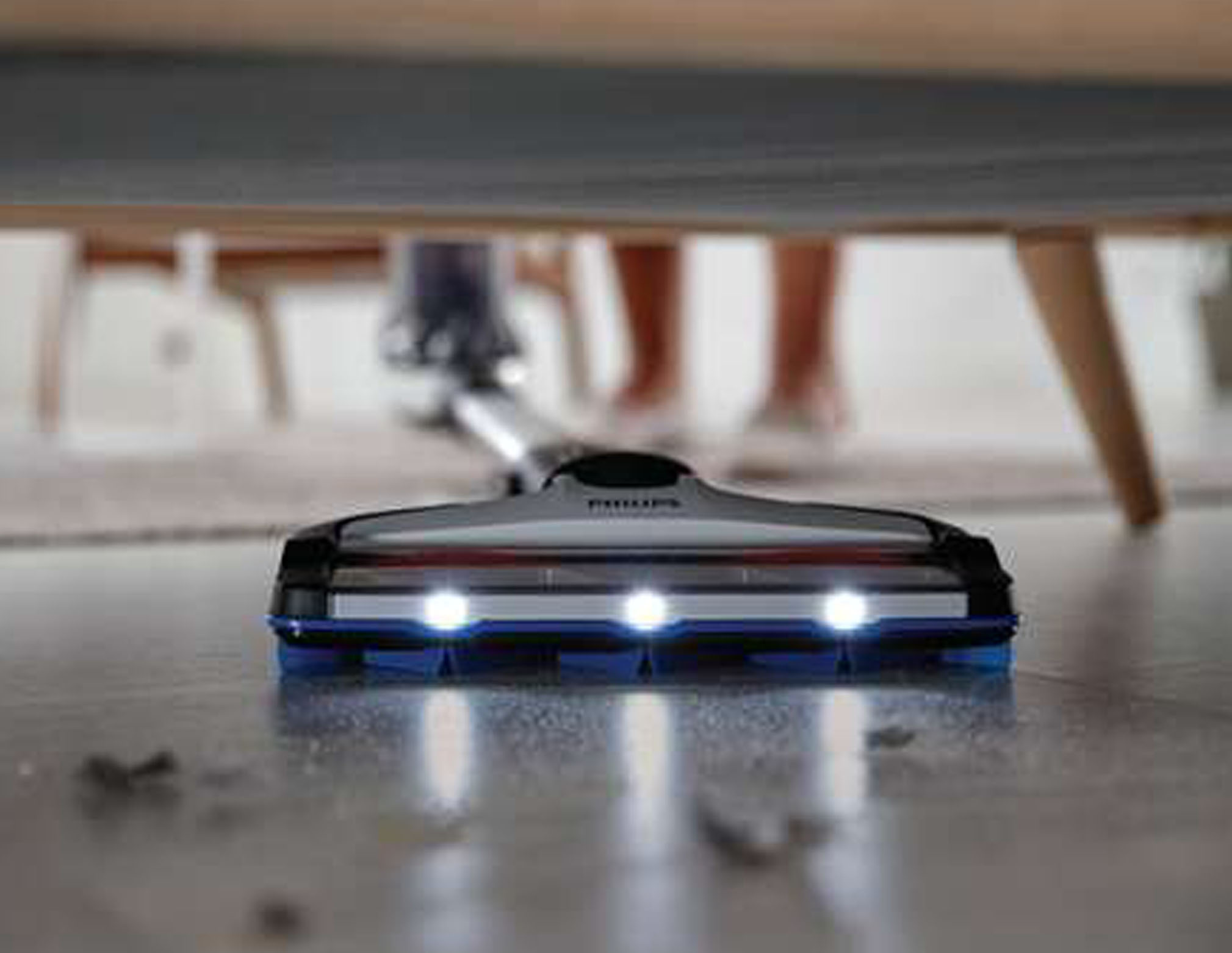 Ein Philips Staubsaugerkopf auf dem Boden. Lichter sind an. Beine von Möbeln und einer Person sind im Hintergrund zu sehen.