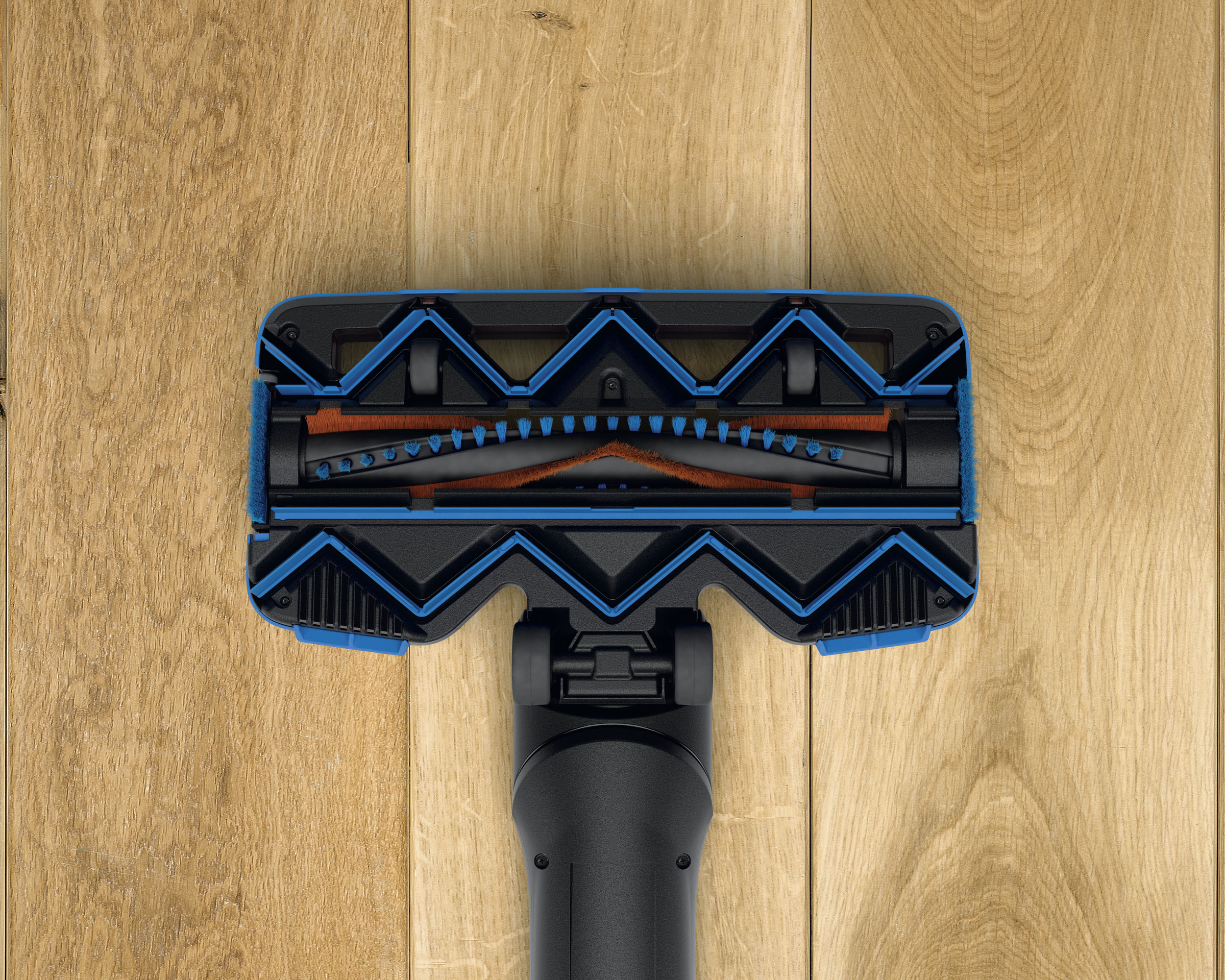 Ein Staubsaugerkopf, blau und schwarz, liegt auf einem Holzboden. Die Bürste ist mit orangefarbenen Borsten sichtbar.