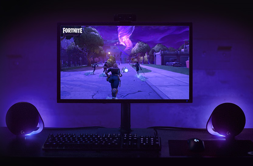 A computer monitor showing a Fortnite game. There are speakers and keyboard.
