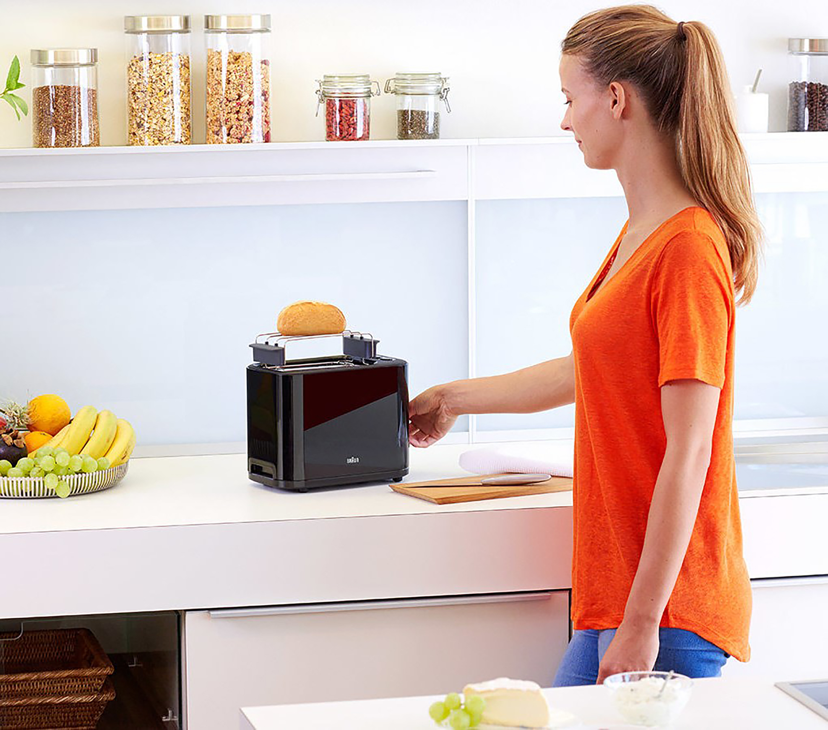 Frau benutzt schwarzen Braun-Toaster. Brot wird getoastet. Küchenarbeitsplatte.