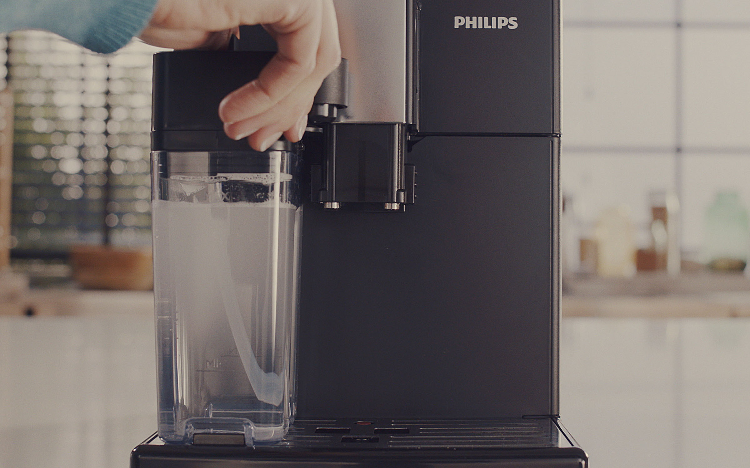 Hand, die Wasser in eine schwarze Philips-Kaffeemaschine gießt, weißer Hintergrund.