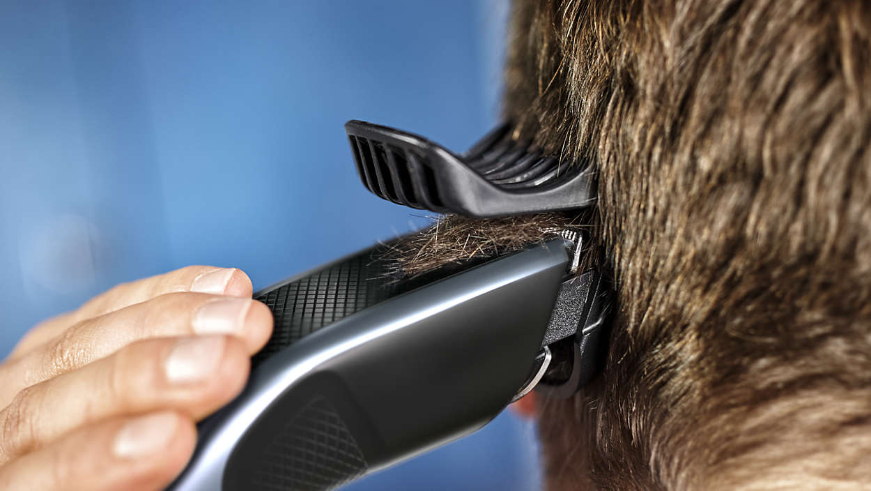 Mann schneidet Haare mit einem schwarzen und silbernen Trimmer.