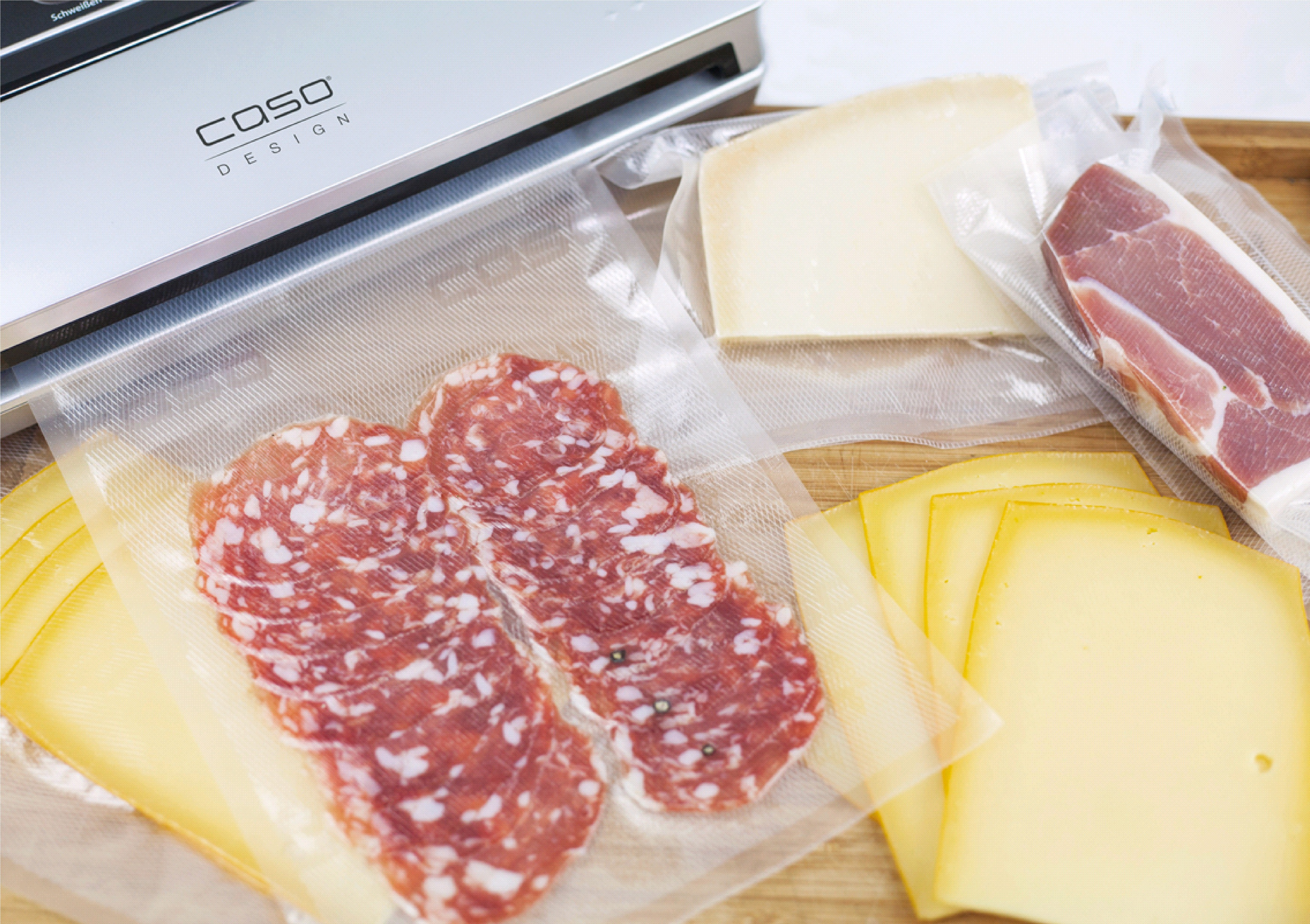 Vakuumverpackte Lebensmittel: Salami, Käse und Schinken auf Holzbrett.