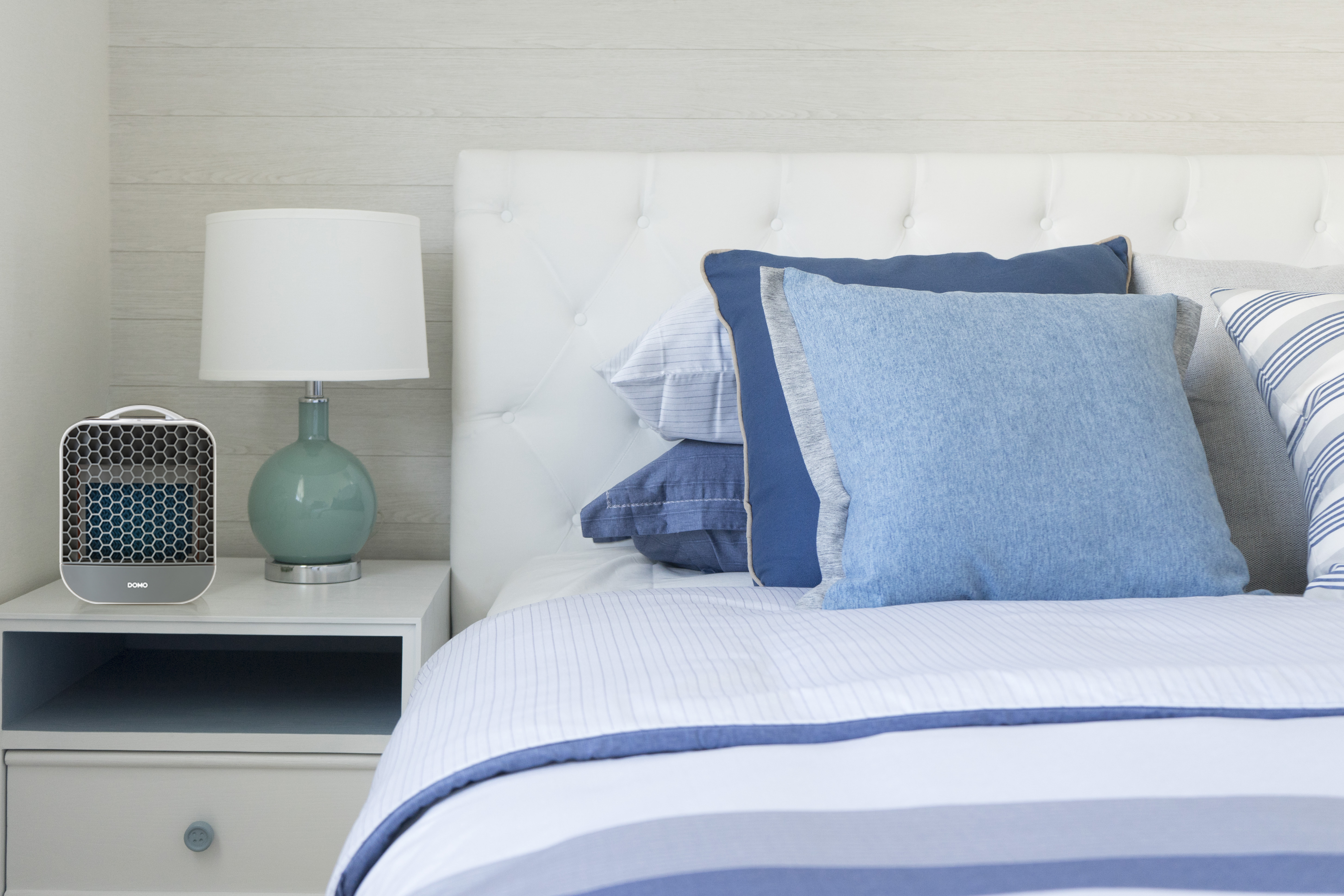 Scène de chambre avec un lit, des oreillers, une lampe et un purificateur d'air. Le lit a une literie bleue et blanche. La lampe est verte.