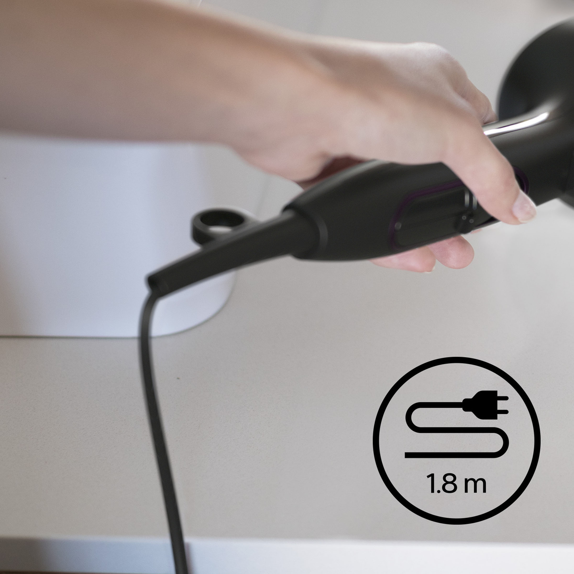 Eine Hand hält einen Haartrockner. Das Kabel hat ein Steckersymbol mit 1,8 m Text.