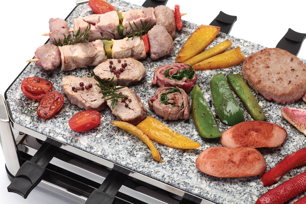 Vari cibi grigliati su una griglia in pietra, tra cui carne, verdure e salsicce.