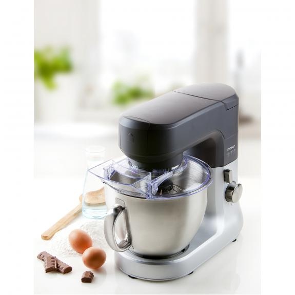 Silver mixer with black top, clear bowl, and ingredients. Set on a kitchen counter.